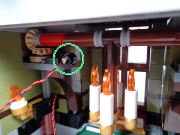 As shown by the green circle in the first photo for this step, pass the plug through the hole in the black LEGO plate you mounted earlier, and pull the wire through the hole so there is minimal slack back down the door hinge.