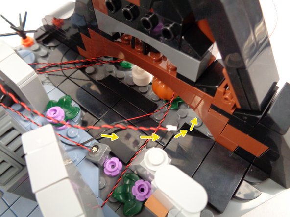 As shown by the yellow arrows in the second photo for this step, pass the LED light wires back and under the wave frame.