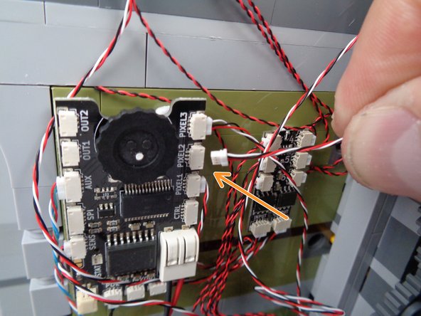 As shown by the orange arrow and circle in the photos for this step, connect the light strip wire to the plug labeled &quot;PIXEL2&quot; on the main effect controller.