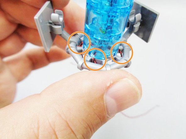 Carefully run the wires down to the bottom of the gray piece and through the gaps as shown by the orange circles.
