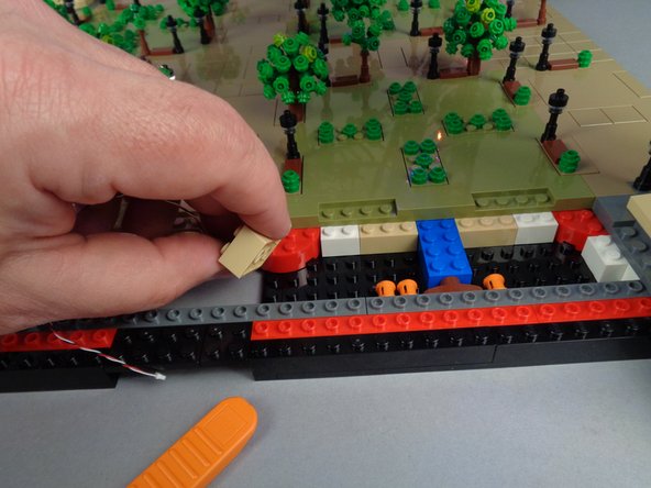 As shown in the photos for this step, remove the 2x3 tan brick under Panel 2F and run the control cable between the studs on the black bottom plate, then re-attach the tan brick on top of the cable.