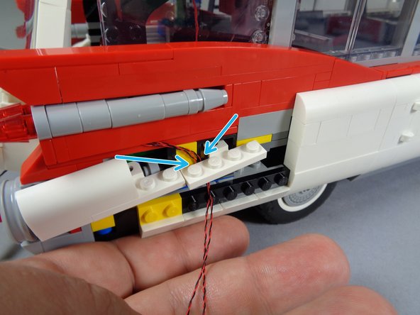 As shown by the blue arrows in the first photo for this step, pass the two light wires behind the white bracket attached to the car's frame.