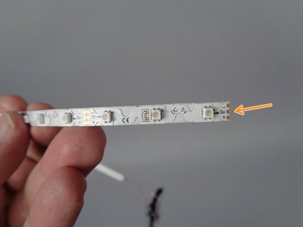 As shown by the orange arrow in the first photo for this step, look for the end of the strip without the wire attached.  This is the part of the strip you will place into the bottom of the elevator shaft.