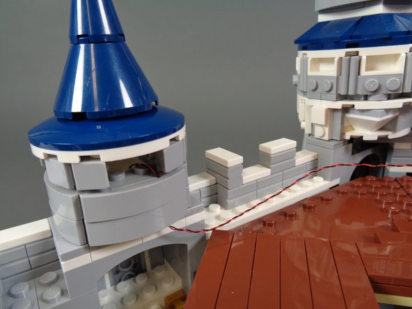 As shown in the photos for this step, carefully re-assemble the first tower, making sure the LED light wire runs between, not on top of, any studs.