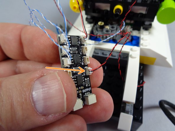 As shown by the green arrows in the first photo for this step, route the light wire for the rear interior light around the side of the roof and through one of the holes in the light bluish gray Technic brick on the roof.