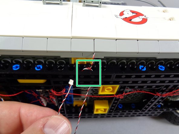 As shown by the green rectangle in the first photo for this step, pass the door switch wire through the holes in the black Technic frame and loop it several times to provide strain relief.