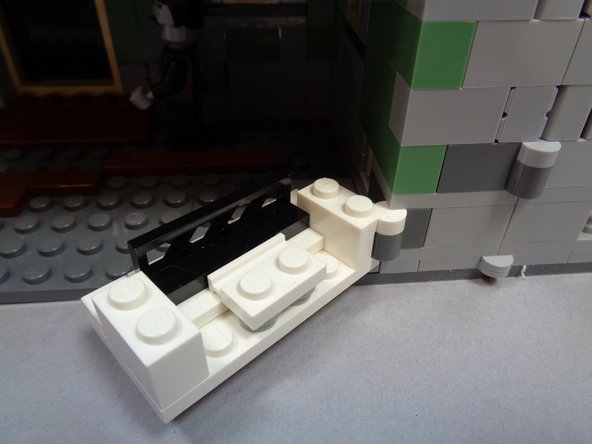 As shown in the photos for this step, re-assemble the fireplace and re-attach it to the wall-mounted hinge beginning with the bottom of the fireplace.