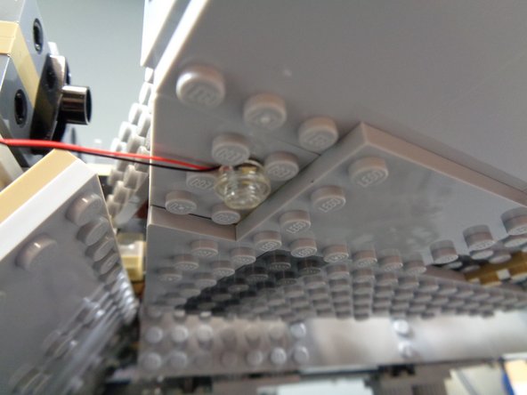 As shown in the third photo, with the light positioned between four studs, you can then attach one of the clear round LEGO plates (included in the landing lights bag) on top of the light.