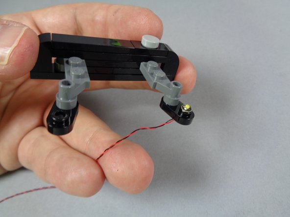 As shown in the second photo for this step, gently pull the light wire all the way through the hole so the LED light sits directly on top of the open stud of the black strobe mount.