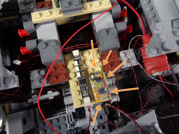 As shown by the orange arrows in the photo for this step, mount the RF remote receiver on the right side of the tan plate, next to the BRANCH09 adapter board you attached earlier.