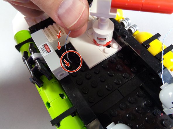 As shown by the red arrows and red circle in the first photo for this step, pass the plug for the red light wire down through the hole in the black plate of the roof assembly.