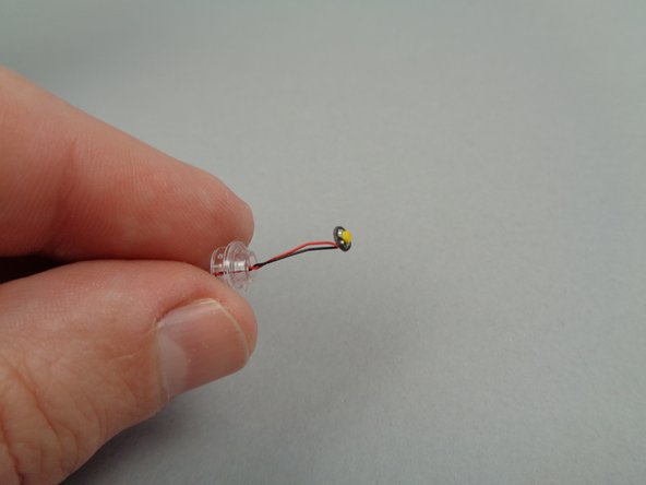 As shown in the second photo for this step, take the last remaining LED light from the bag with the orange dot and pass its wires through the hole in the 1x1 round transparent plate.