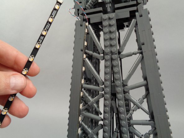 Remove the backs of the sticky dots on the second light strip (connected to plug #2 of the adapter board), and attach the strip to the tower frame as shown in the photos for this step.