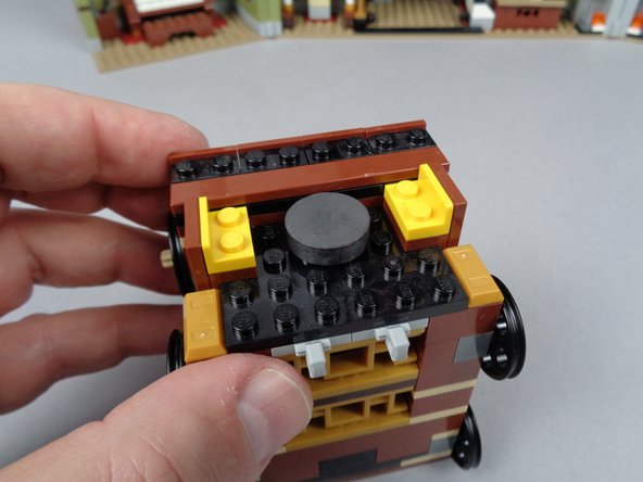 As shown in the photos for this step, remove the adhesive from the back of the magnet, and stick it to the center of the elevator between the two yellow LEGO brackets.