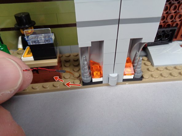 Making sure the flexible wire runs between and not on top of any studs, carefully re-attach the fireplace section in the mansion as shown in the second photo for this step.