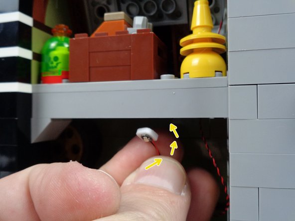 As shown by the yellow arrows in the first photo for this step, attach the green LED light to the ceiling under the attic floor.  The light should be attached so it is behind the front long brick, so it is not easily visible when looking at the inside of the mansion.