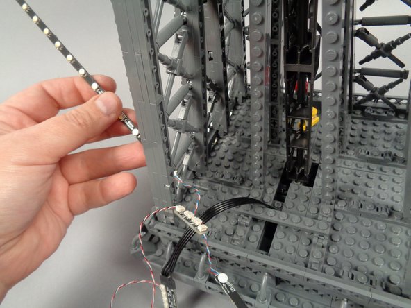 As shown in the second and third photos for this step, take the light strips connected to plug #1 on the adapter board and pass them through the first tower pillar.