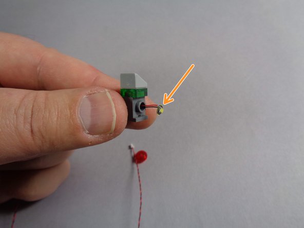 As shown by the orange arrow in the second photo for this step, carefully bend the round LED light board so it will sit flat on top of the hole in the brick.