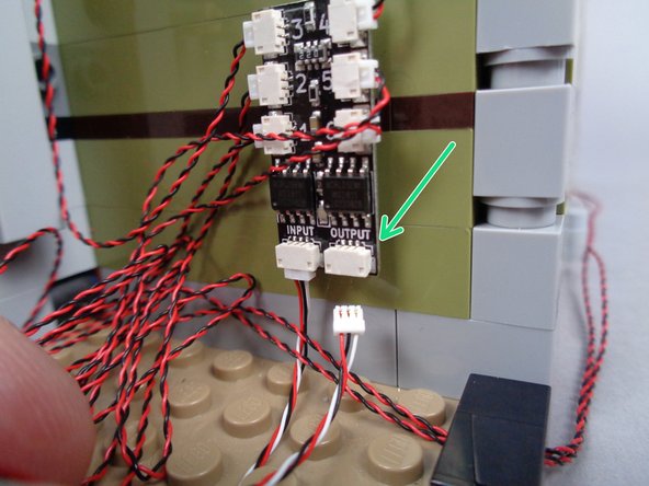 As shown by the green arrow and rectangle in the photos for this step, connect one end of the 3-wire connecting cable to the OUTPUT plug on the second BRANCH06X adapter board (the board you recently finished connecting lights to).