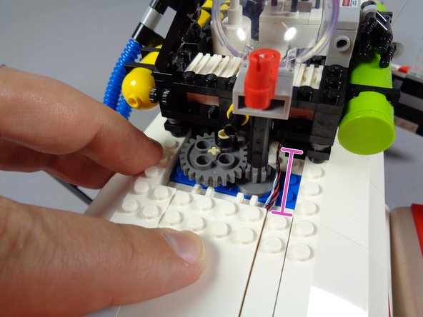 Press down on the white roof slope to fit it back into place.  As shown by the pink line in the third photo, check again to make sure all wires pass along the outside of the roof gears.