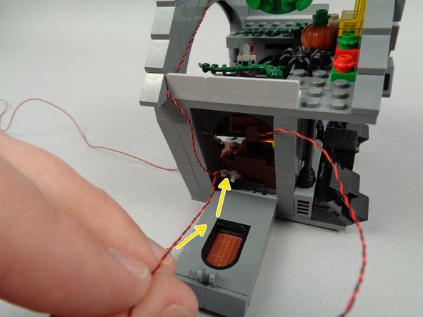 As shown in the first photo for this step, pass the light wire for the blackboard light back under the desk and out through the back of the house as shown in the second photo.