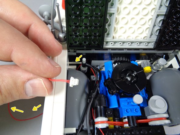 As shown by the yellow arrows in the second photo for this step, pass the red wire down behind the wheel well and out the side, behind the front wheel.
