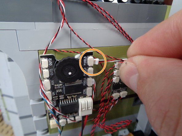 As shown by the orange circle and arrow in the photos for this step, connect the other end of the 3-wire connecting cable to the plug labeled PIXEL3 on the main effect controller.
