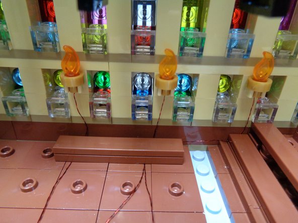 As shown in the third photo, carefully re-attach one of the brown benches on top of the wires for the first three torches.