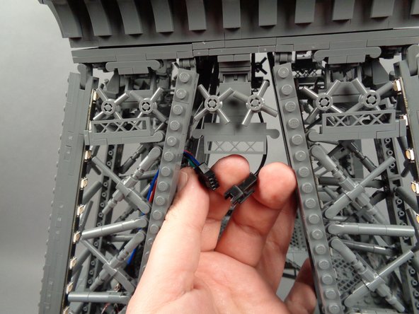 As shown by the yellow arrows in the first photo for this step, carefully place the top tower section on top of the middle section, being careful to pass the wire and plug through the gap in the middle rear tower frame.