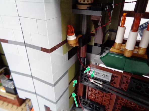 As shown by the green arrows in the second photo for this step, use the tweezers to coil the light wire around the front door hinge 2-3 times and up toward the top of the door like you did with the fireplace wire earlier.