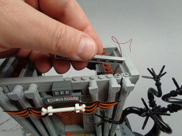 As shown in the photos for this step, re-attach the two long tiles to the top front of the town hall.