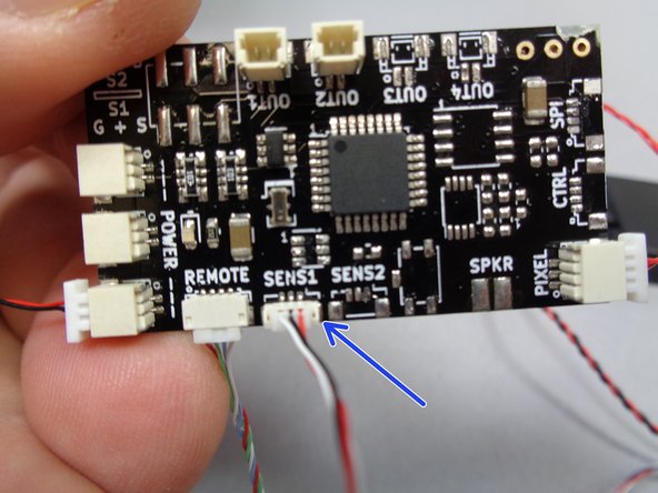 As shown by the blue arrow in the second photo, connect the red/white/black control wire with the small connector to the plug on the TRUNK08 master controller labeled &quot;SENS1&quot;.