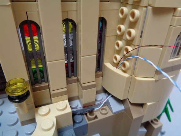 As shown in the first photo, run the two torch wires up the side of the castle tower and re-attach the first tan slope part so it covers the wires.