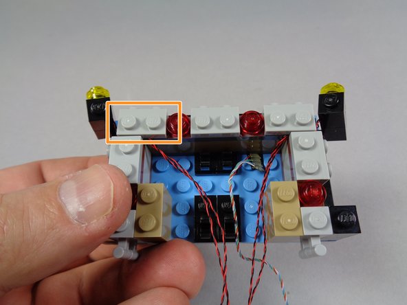 As shown by the orange rectangle in the second photo, carefully re-attach the gray bracket so the wires pass underneath.  The bracket should hold the wires, and the two black bricks, in place.
