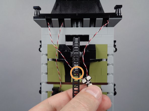 As shown by the orange circle in the second photo for this step, make sure the wire for the left-side light strip passes behind the elevator chain, not in front of it.  This is critical to prevent the chain from pulling or catching on the wire.