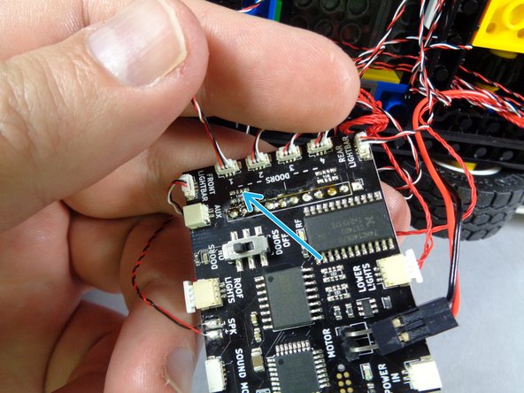 As shown by the blue arrow in the third photo for this step, connect the fourth door switch to the last available DOORS plug on the main controller.