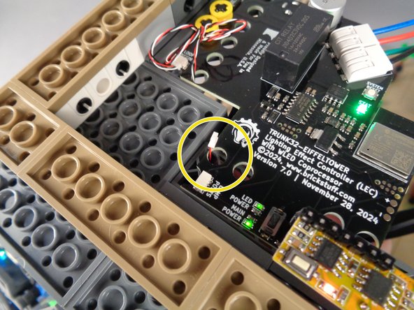 As shown by the yellow circle in the second photo for this step, carefully pass the control cable under the main controller and through the hole in the board next to the &quot;LAMP POSTS&quot; plug.