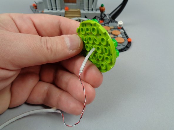 As shown in the first two photos for this step, pass the end of the light strip (the short segment) though the bottom center of the fountain base.