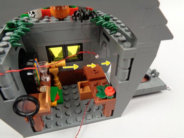 As shown by the yellow arrows in the first photo for this step, pass the light wire for the blackboard light back behind the desk and out the wall opening behind the desk.