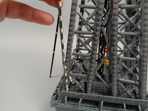 Remove the backs of the sticky dots on the second light strip (connected to plug #2 of the adapter board), and attach the strip to the tower frame as shown in the photos for this step.