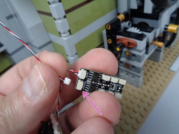 As shown by the purple arrow in the second photo for this step, connect the long 3-wire cable from the front mansion section to the plug on the BRANCH06X adapter labeled OUTPUT.