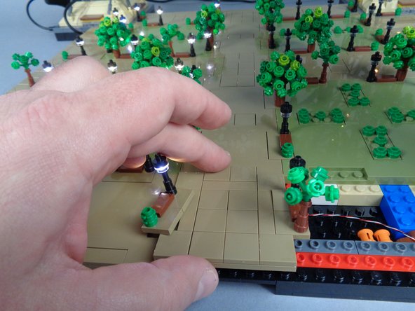 As shown by the yellow arrow in the first photo for this step, carefully lift up the edge lamp post on Panel 2R and its base.  This is to make room to re-insert the small plate.