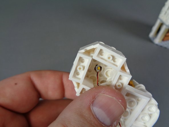 As shown in the first photo for this step, bend the wire on one of the lights and place it down inside the small ceiling area.