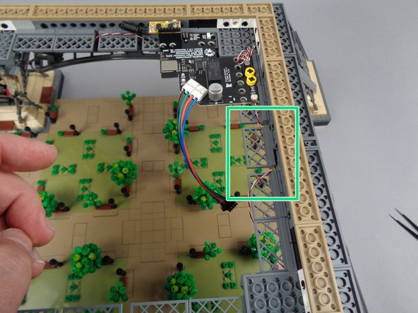 As shown by the green rectangle in the photo for this step, clean up any loose hanging control wires by looping them over the fence elements in the tower frame.