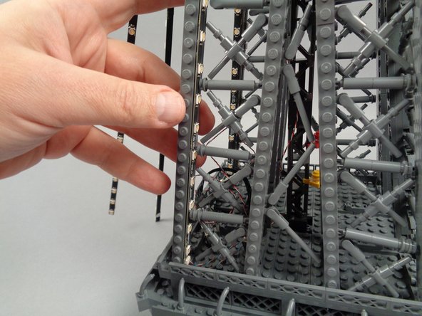 Remove the backs of the sticky dots on the second light strip (connected to plug #2 of the adapter board), and attach the strip to the tower frame as shown in the photos for this step.
