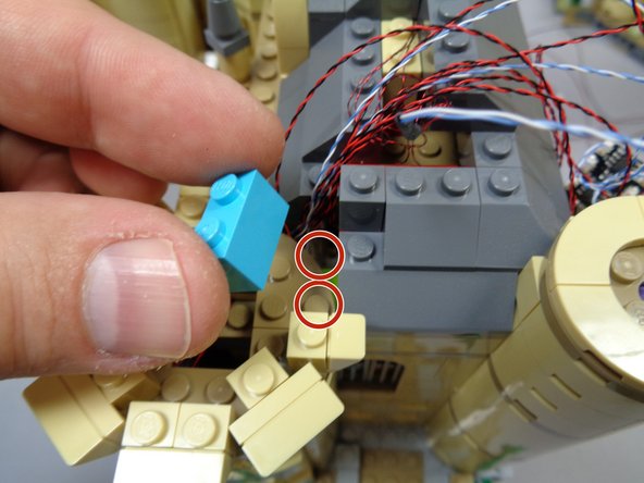 As shown in the third photo, take the light blue brick you removed from the roof earlier and attach it to the area shown by the two red circles.