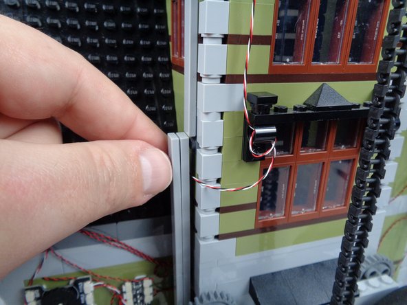 As shown in the photos for this step, finish routing the magnetic switch wire by running it behind one of the long LEGO tiles used to support the tower.