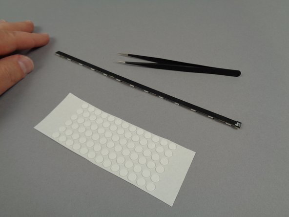 As shown in the photos for this step, use your tweezers to attach four sticky dots to the back of each of the eight 13-LED light strips you will use for the base tower level.