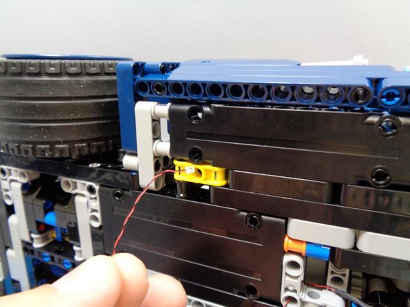 As shown in the third photo, route the wire up and through the hole in the yellow Technic bracket, toward the top of the car.