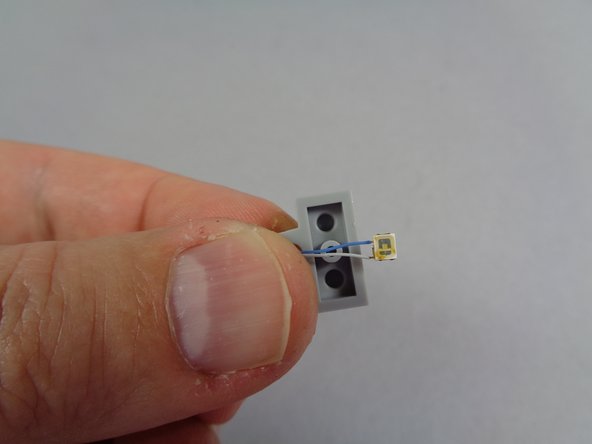 As shown in the second and third photos, position the blue LED light in the center of the 1x2 plate, and carefully re-attach the transparent round blue boat stud on top, making sure no light wires are pinched by any studs.